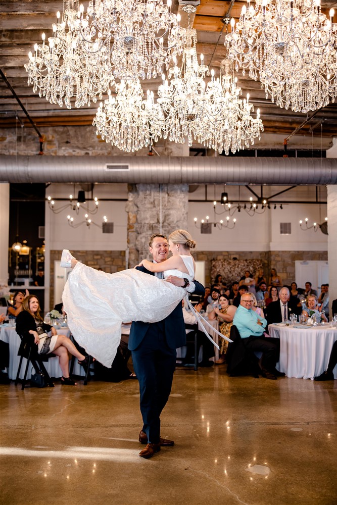 Groom lifting his bride beneath rows of crystal chandeliers during the first dance at Stone Manor on 79th in Overland Park, Kansas