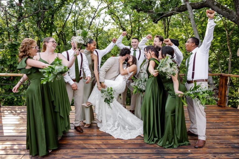 Wedding party cheers with arms raised as the bride and groom kiss on a wooden deck at a private residence wedding in Blue Springs, Missouri