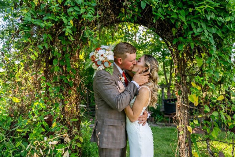 Bride and groom share their first kiss under a draped wooden wedding arbor with pampas and orange roses at Tobacco Barn Farm in Holt, Missouri