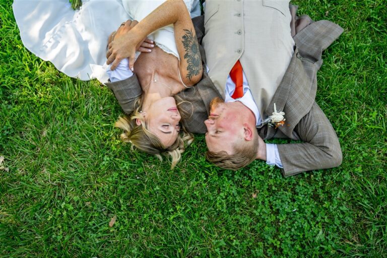 Overhead photo of a bride and groom lying head to head in green clover grass looking at each other at Tobacco Barn Farm