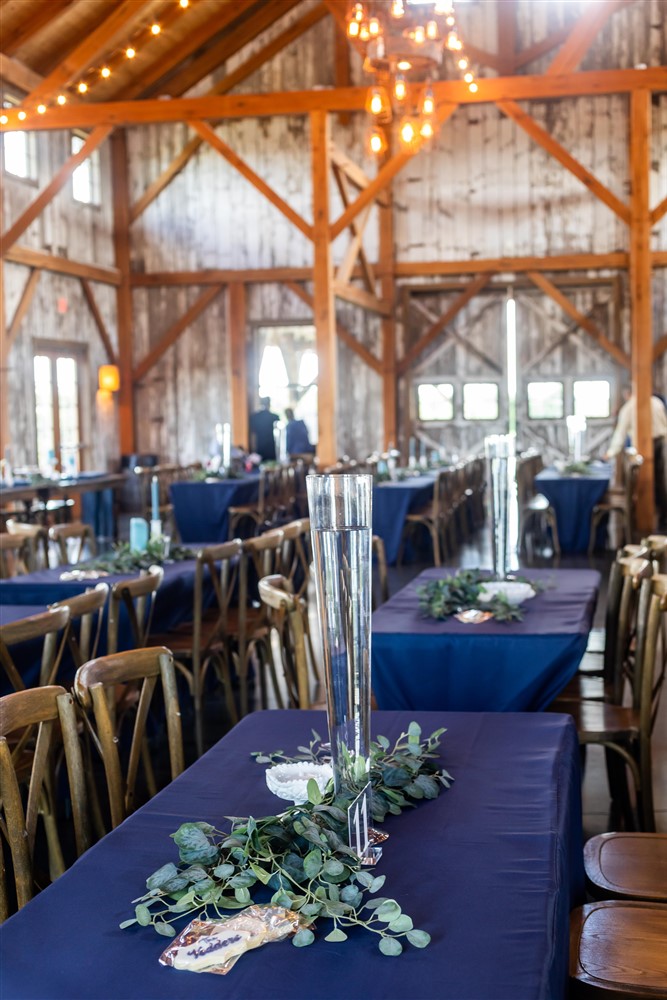 Reception tables set with navy linens, eucalyptus garland and tall glass cylinders inside the barn at Red Barn Farm in Weston, Missouri