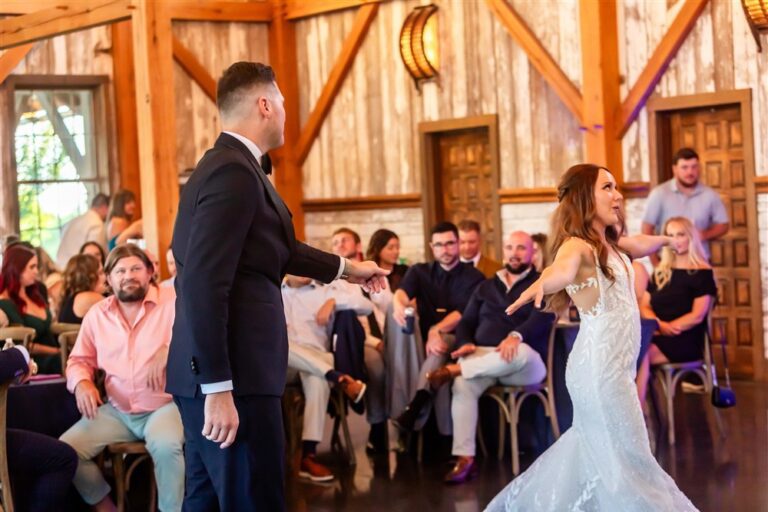Bride and groom dance facing each other in front of seated guests inside the barn at Red Barn Farm in Weston, Missouri