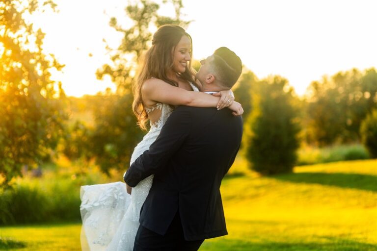 Groom lifts the bride into the air in golden hour sunlight on the lawn at Red Barn Farm in Weston, Missouri