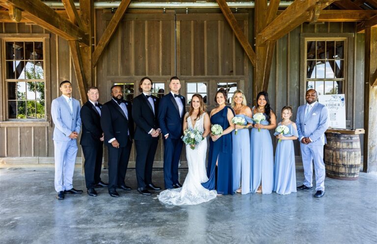 Full wedding party in navy, black and dusty blue lines up under the barn pavilion at Red Barn Farm in Weston, Missouri