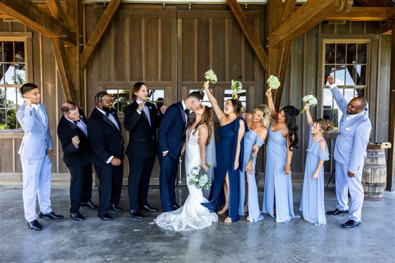 Wedding party cheers and raises bouquets as the bride and groom kiss at Red Barn Farm in Weston, Missouri