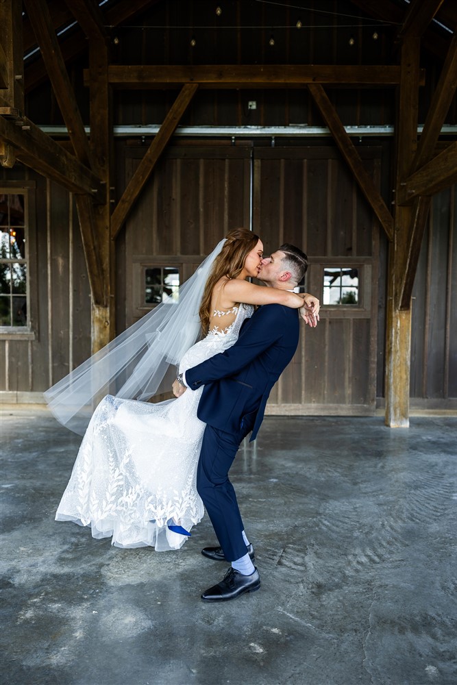 Groom lifts the bride off her feet for a kiss in front of the barn doors at Red Barn Farm in Weston, Missouri
