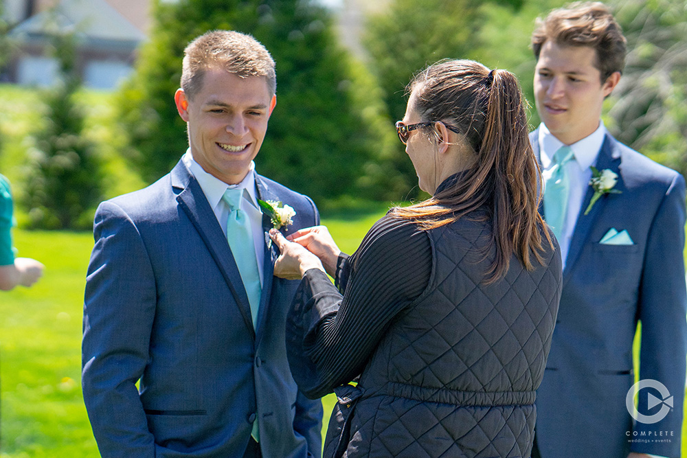 wedding planner putting assisting boutonnière on groomsmen