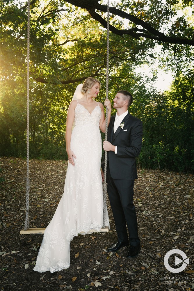 Bride on swing while groom looks up at her during wedding day beautiful photo