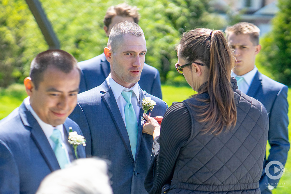 wedding planner putting assisting boutonnière on groomsmen