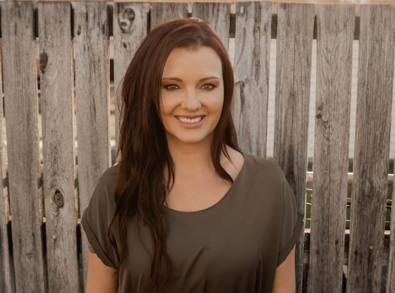 Danielle Wheaton, services consultant and photographer at Complete Weddings + Events, smiling in front of a rustic wooden fence.