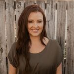 Danielle Wheaton, services consultant and photographer at Complete Weddings + Events, smiling in front of a rustic wooden fence.
