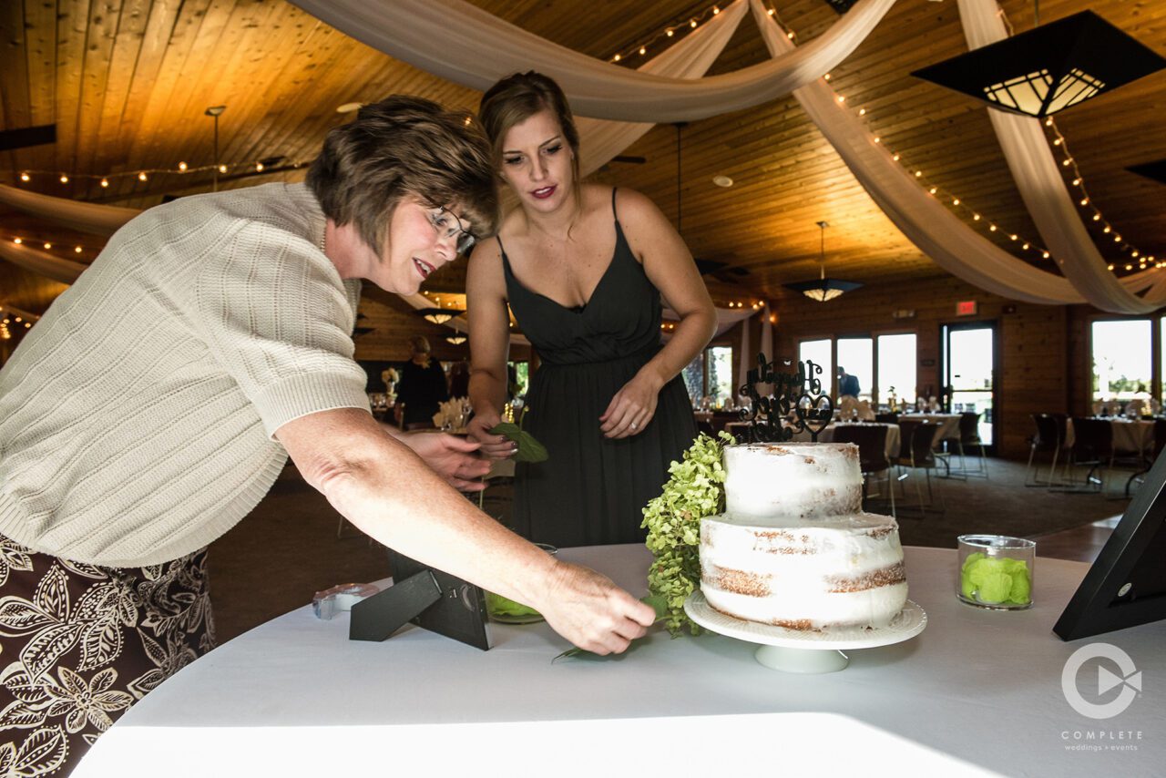 Complete Weddings + Events coordinator assists a bridesmaid to make sure the cake is photo-ready.