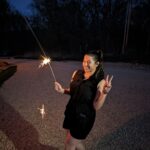 Nashville wedding DJ and photographer, Laura Garotti, poses at the end of a successful wedding with a sparkler in hand and putting up a peace sign with her other hand.