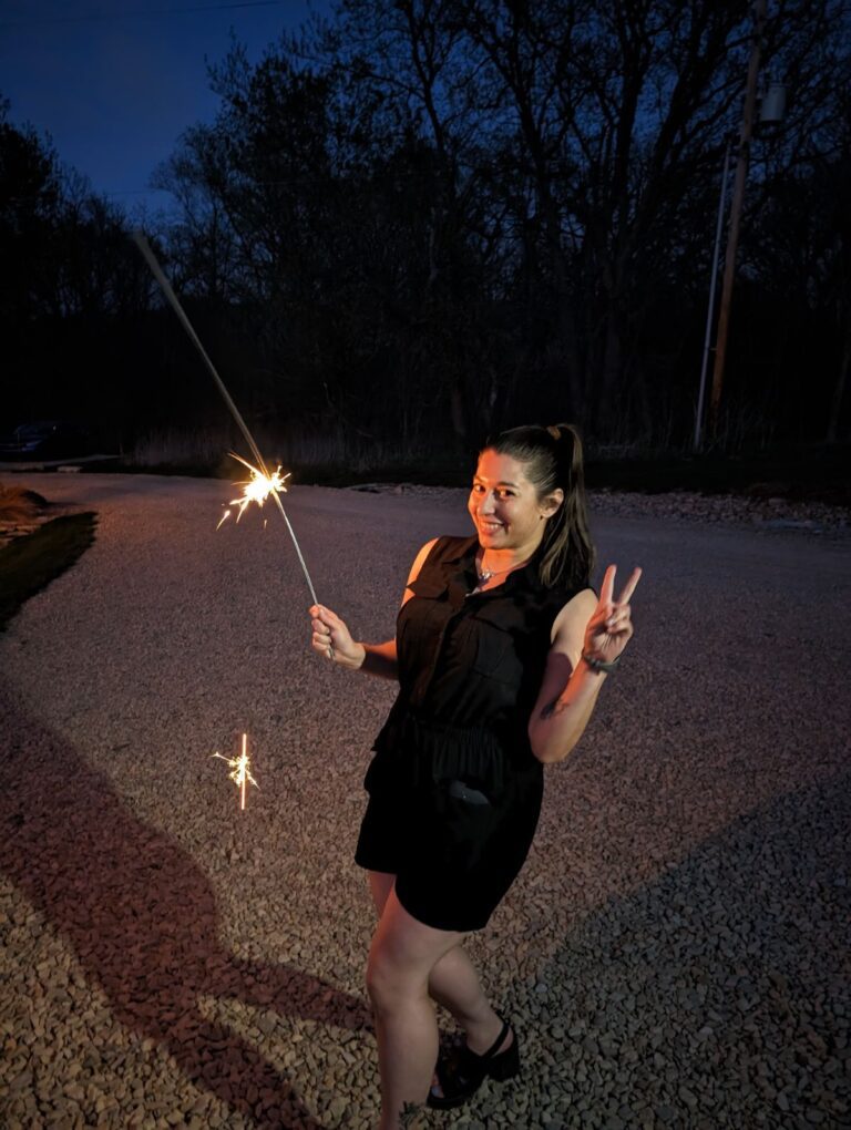 Nashville wedding DJ and photographer, Laura Garotti, poses at the end of a successful wedding with a sparkler in hand and putting up a peace sign with her other hand.