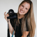 This image shows Anna Mahoney, the lead wedding content creator at Complete Weddings and Events. She has long blonde hair and is holding her DSLR camera while smiling.
