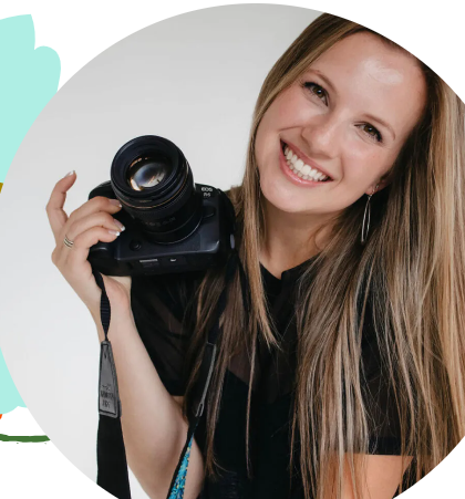 A photo of Nashville wedding photographer Anna Mahoney holding her camera and smiling at the camera in a professional headshot.