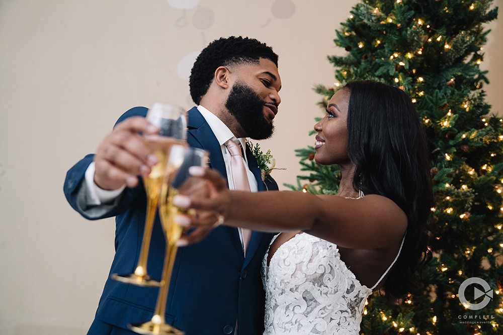 bride and groom toast in front of christmas tree