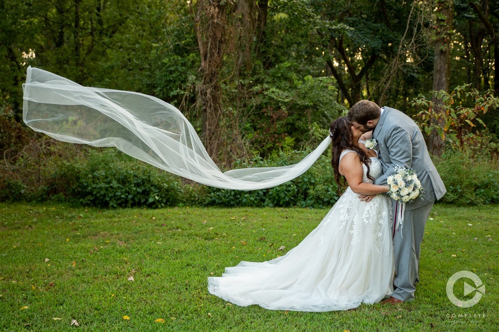 bride and groom kissing with incredibly long veil blowing in the wind