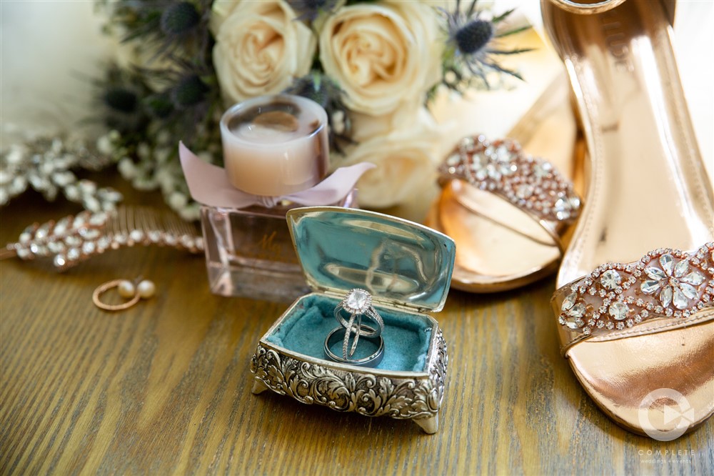 macro shot of decorative wedding ring box with brides bouquet and shoes during a Kindred North wedding