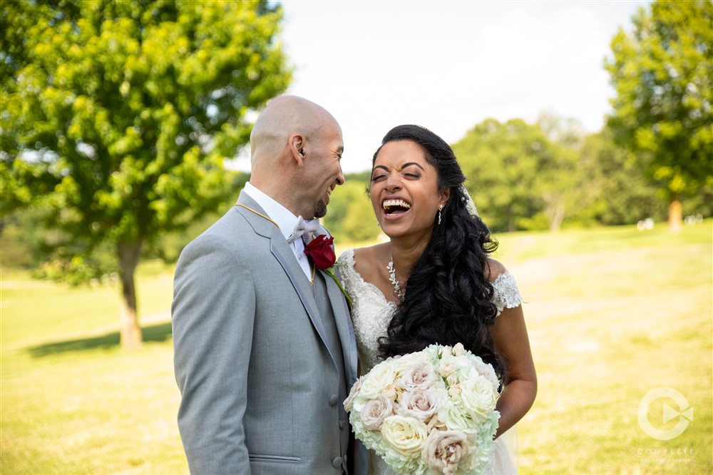 bride and groom laugh together in field