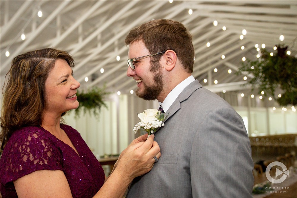 Groom and mother laugh while corsage is being pinned