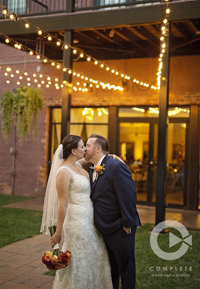 bride and groom kiss under string lights