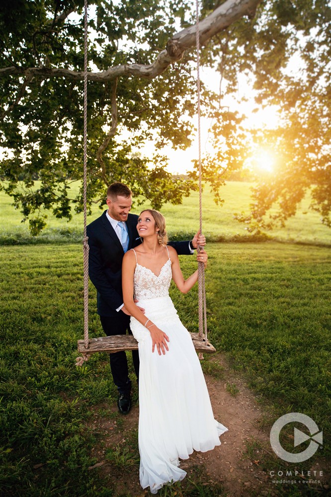 groom pushes bride on swing at sunset