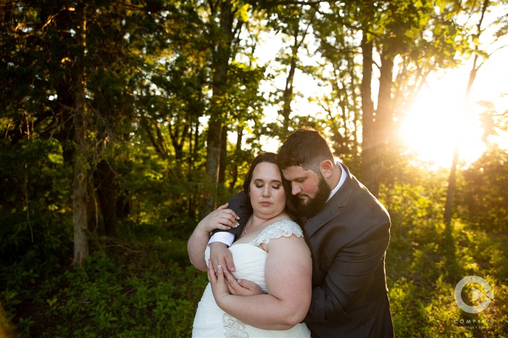 groom hugs bride at sunset in the woods