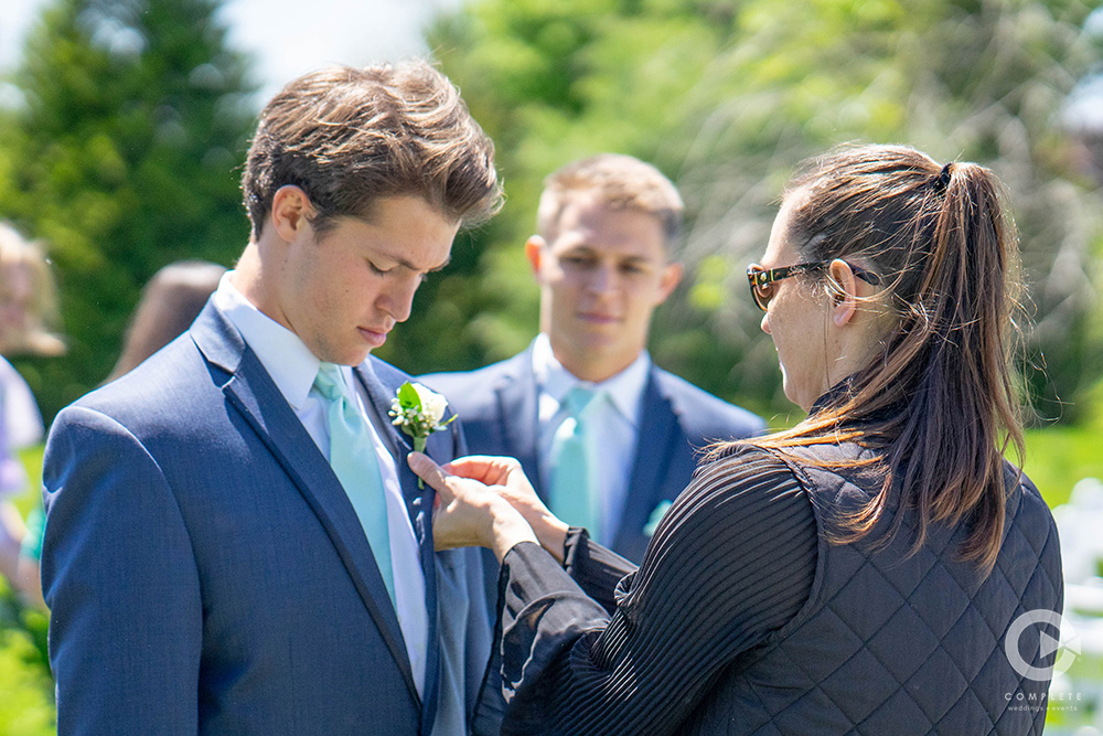 wedding planner putting boutonnière on groomsmen