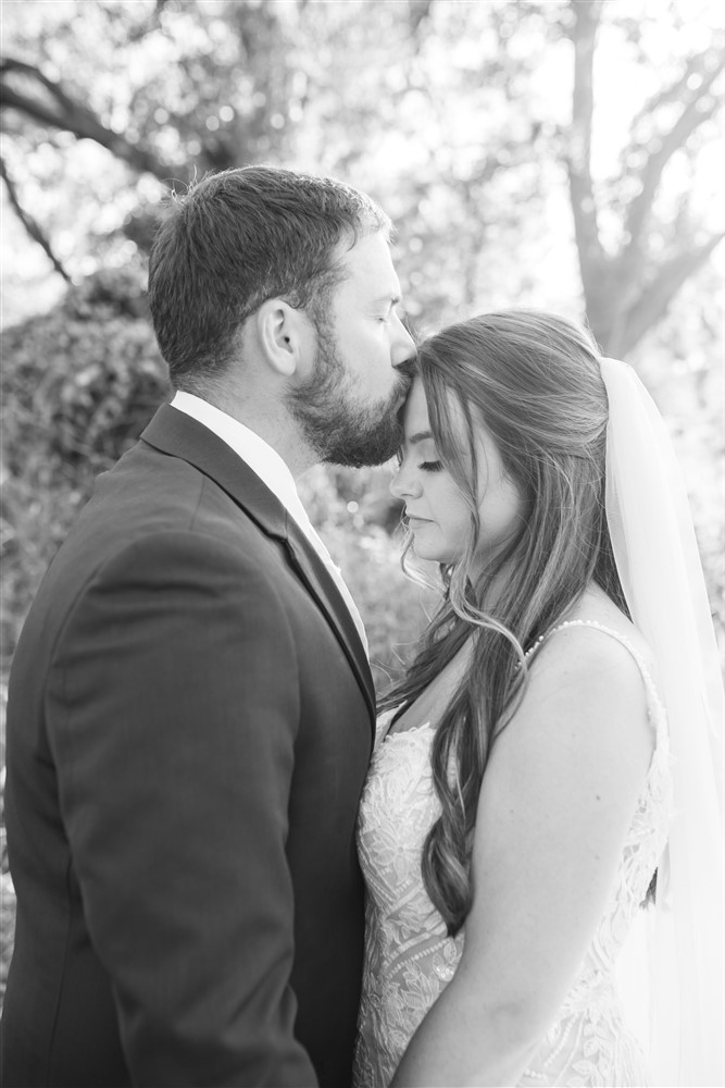 groom giving the bride a forehead kiss photo at the Farmhouse venue outside of Omaha with wedding photographer Cassie Burley