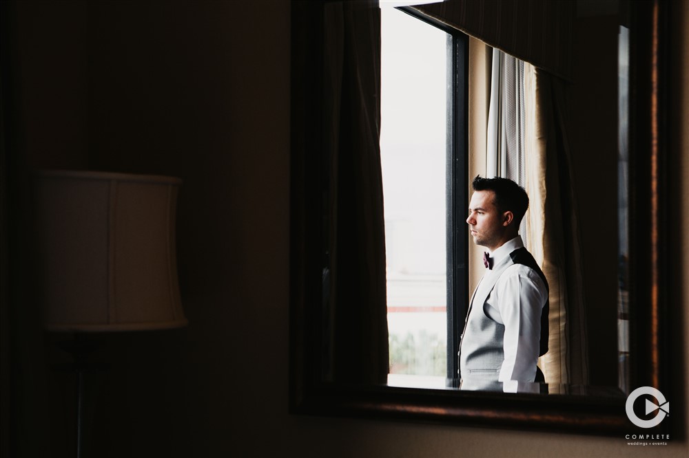 Late Fall time wedding groom looking out of Orlando hotel wedding window while getting ready