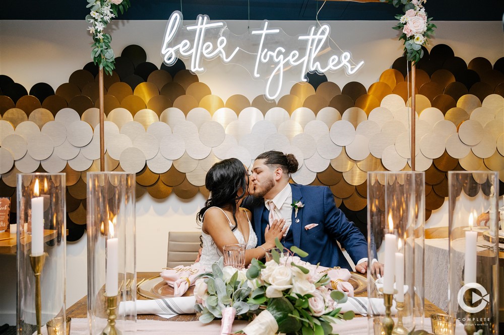 Bride and groom kissing at the head table with better together sign