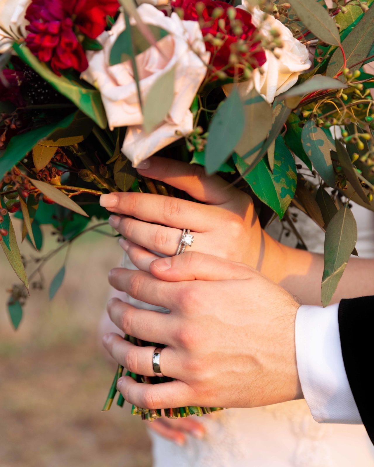Wedding bouquet with bride and groom's hands showing off wedding rings