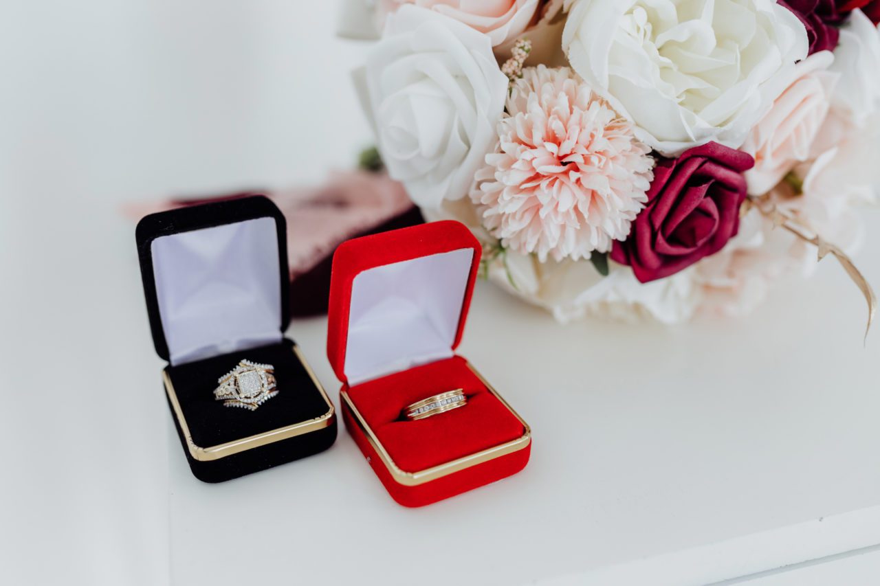 Black and white wedding ring boxes bringing out some beautiful details in each wedding ring with bouquet in the background