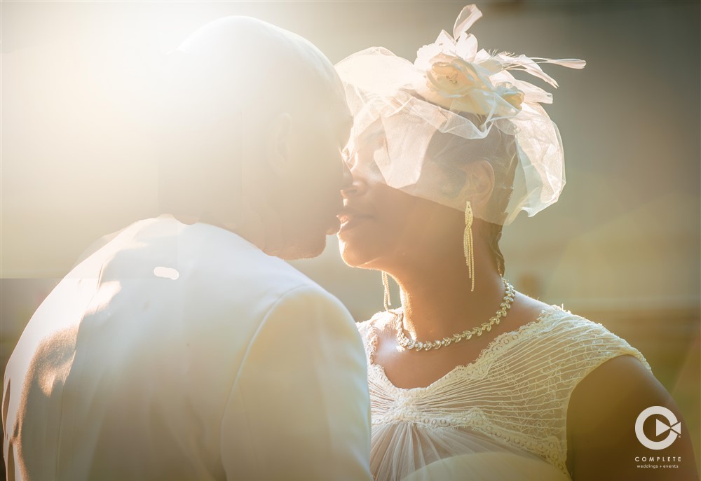 Wedding photo of a couple while the sun shines through the top left corner of the shot