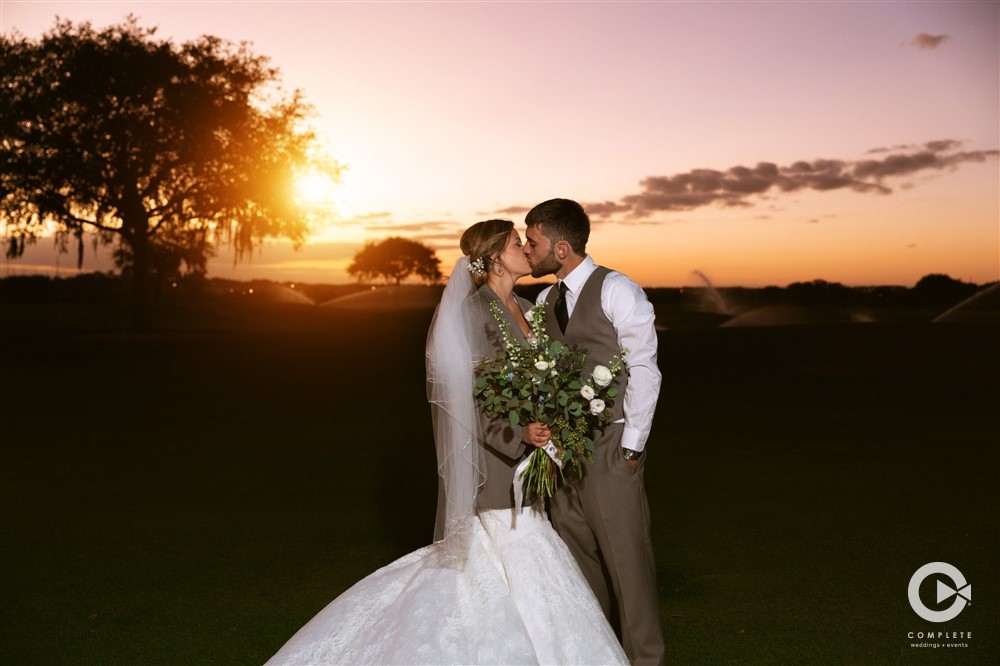 Bride and groom kissing while sun sets behind them during a wedding in the winter