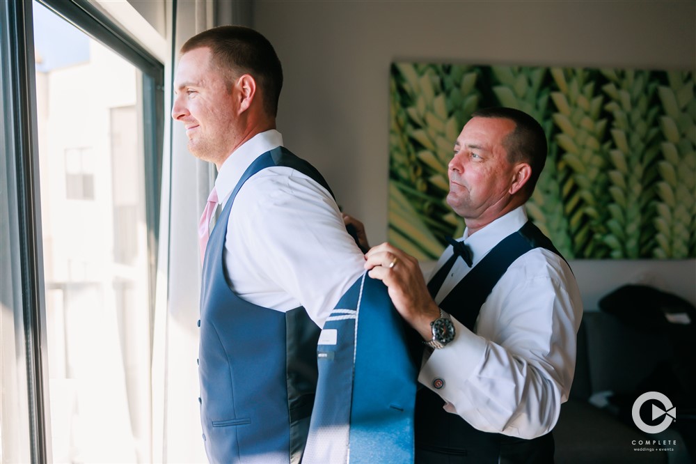 Reunion Resort groom putting on his suit jacket while his father helps him put it on