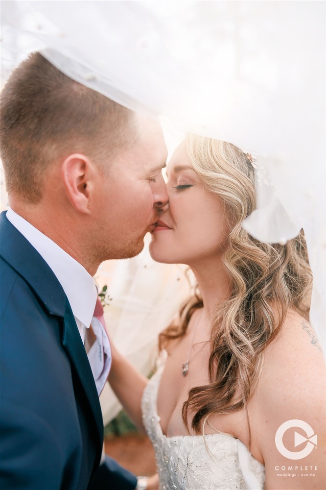 Wedding couple kissing on their big day with the wedding dress veil covering them amazing wedding photoshoot