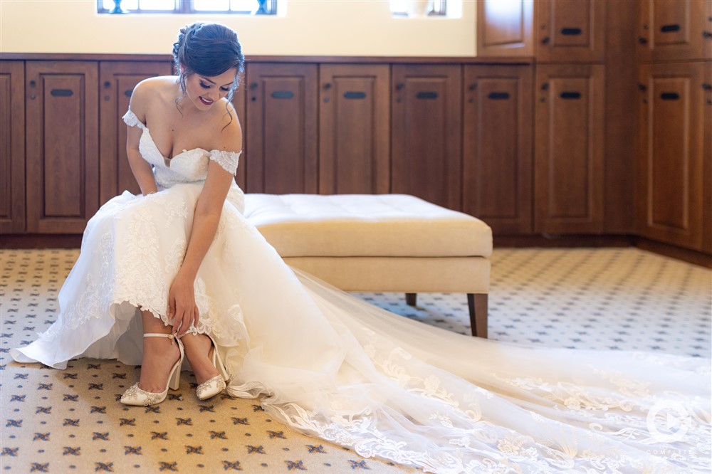 Bride puts on her wedding shoes as her wedding dress sprawls out over the room