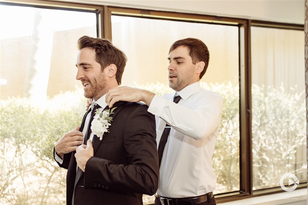 Groom getting ready while best man puts jacket on the groom at his wedding