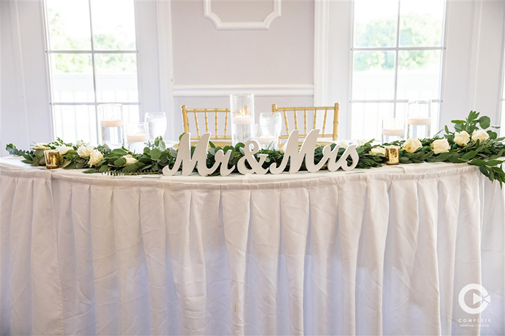 Greenery and gold accents on head table at wedding reception in Orlando, FL