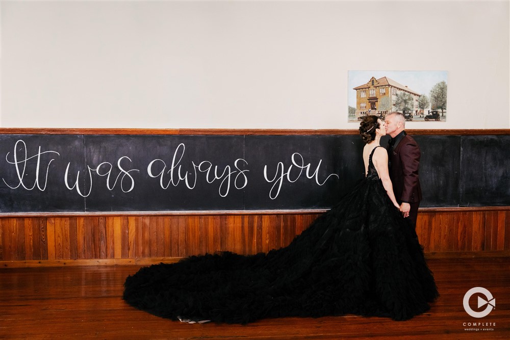Bride and groom kissing in front of blackboard wedding quotes.