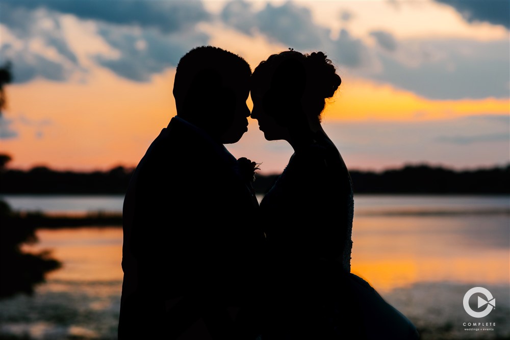Bride and groom shadowed in front of a beautiful sunset at Lake Mary Event Center