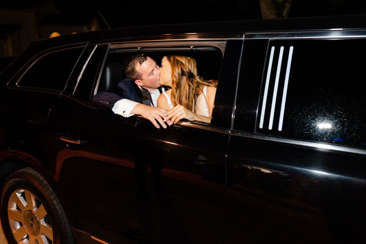 Bride and groom kissing in their limousine getaway car