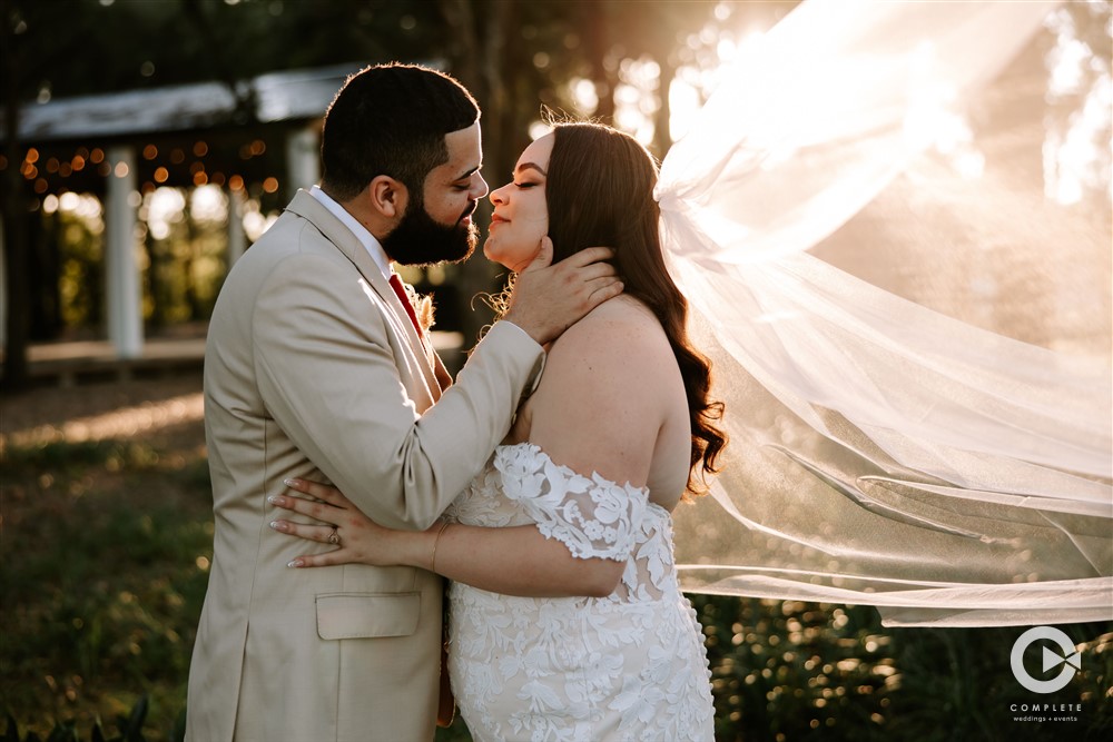 Bride and groom kissing at their wedding in Orlando, FL veil flowing while sun shines through fabric