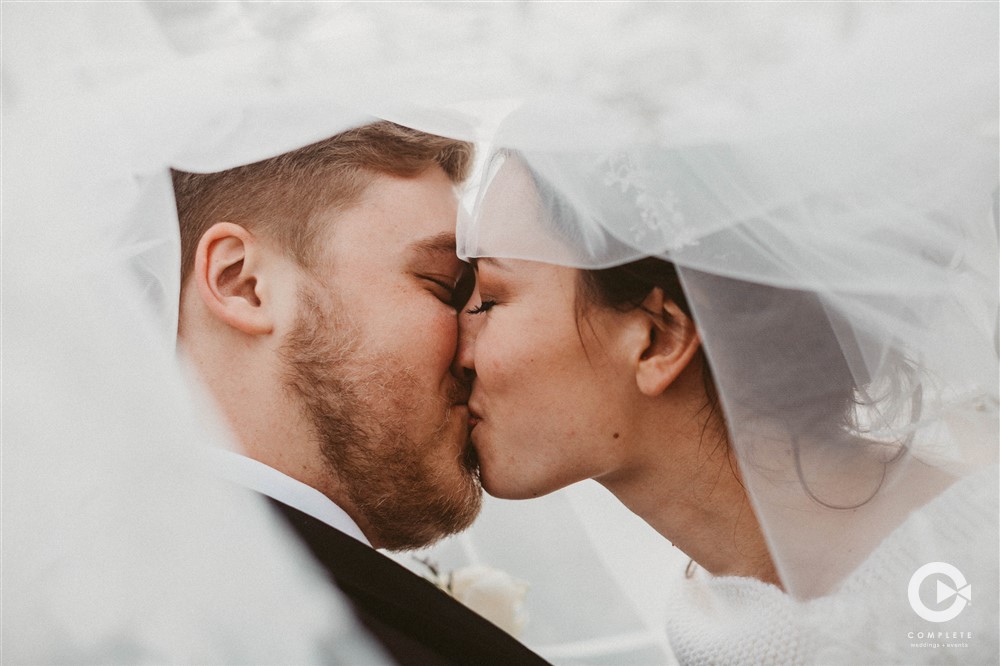 Bride and groom kiss while under bride's wedding veil amazing detail two photographers