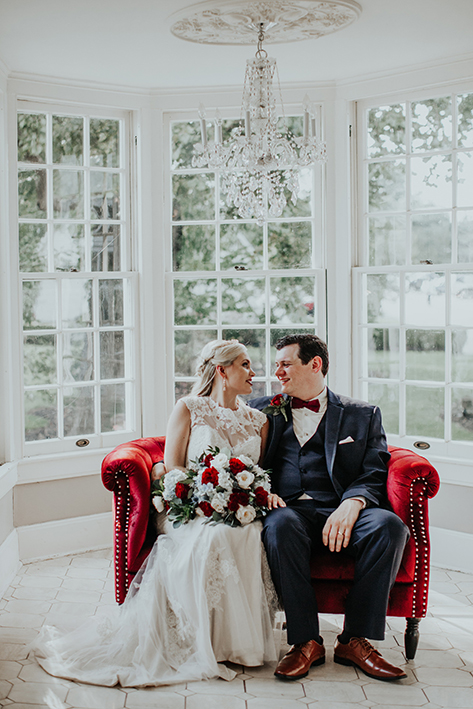 Bride and Groom sitting on red couch at Haseltine Estates