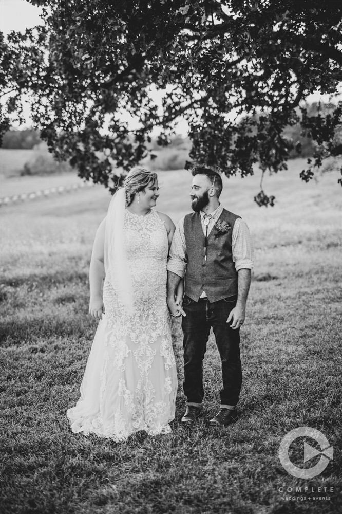 bride and groom smiling at each other under a tree black and white