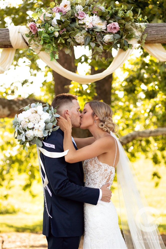 groom and bride kiss under trellis