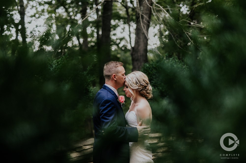 groom kisses bride's forehead in a garden